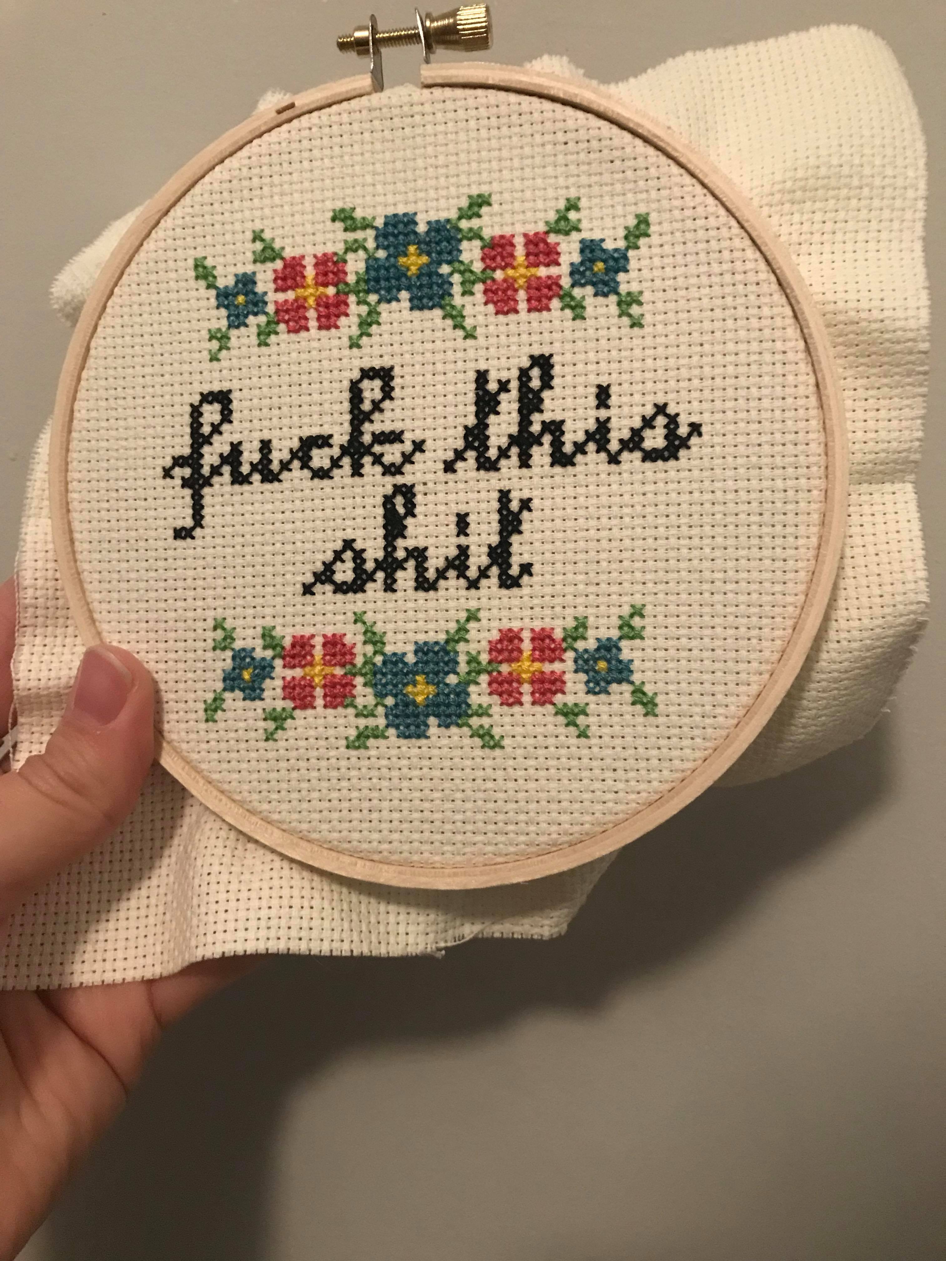 A cross stitch with pink and blue flowers above and below the words fuck this shit